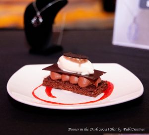 Decorated brownie with brown colored cream, chocolate and whipped cream. Raspberry sauce is drizzled around the brownie.