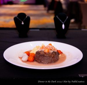 Portion on steak with a lobster tail sitting on top, sauce drizzled around steak with neatly cut up vegetables surrounding it. 