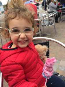 Pictured: Preschooler Vittoria “Vicky” Cerolini in a bright red jacket and eyeglasses, enjoying an outdoor cafe. Vicky has Leber congenital amaurosis (LCA). 