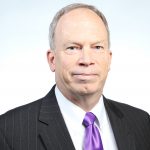 headshot of man in suit and purple tie