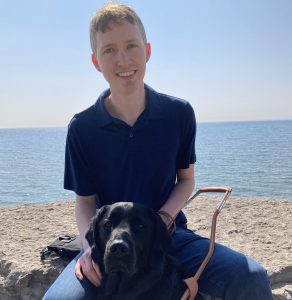 Young man sits with black dog at beach