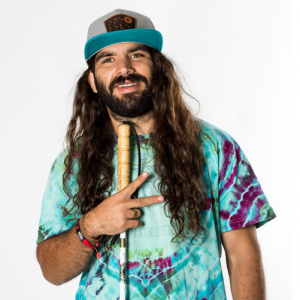 Anthony wearing a tie-dye tee-shirt holding up a peace sign and his guide cane.