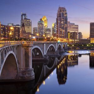 Minneapolis city skyline at dusk with bridge over river.