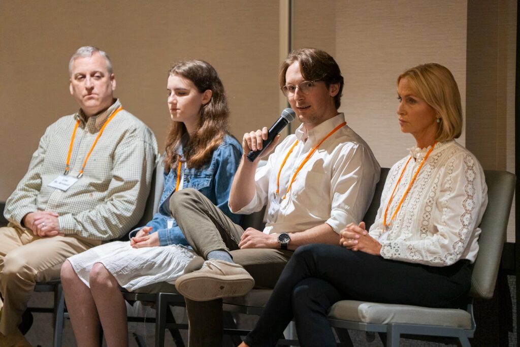 Panelists seated on stage during a clinical trial discussion, with Jack Morris speaking into a microphone