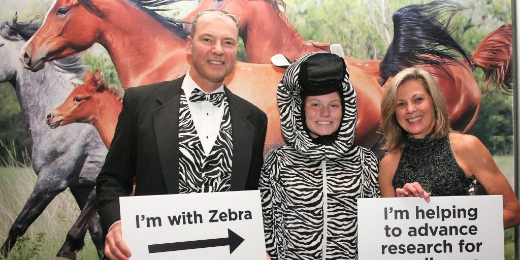 Our iconic zebra with two Dinner in the Dark guests, holding up signs at our photo booth