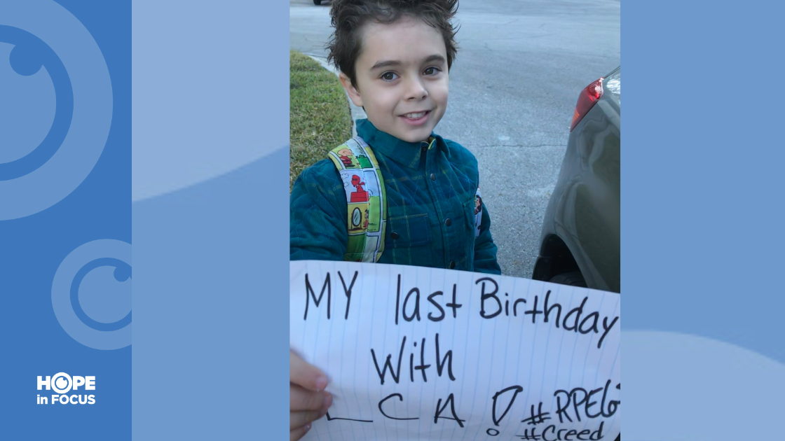 Creed smiling and holding up a piece of paper that writes, "My last birthday with LCA! #RPE65 #CREED