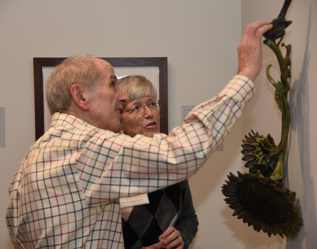 Joe in a stripped shirt holding his hand out to touch something with Alice next to him