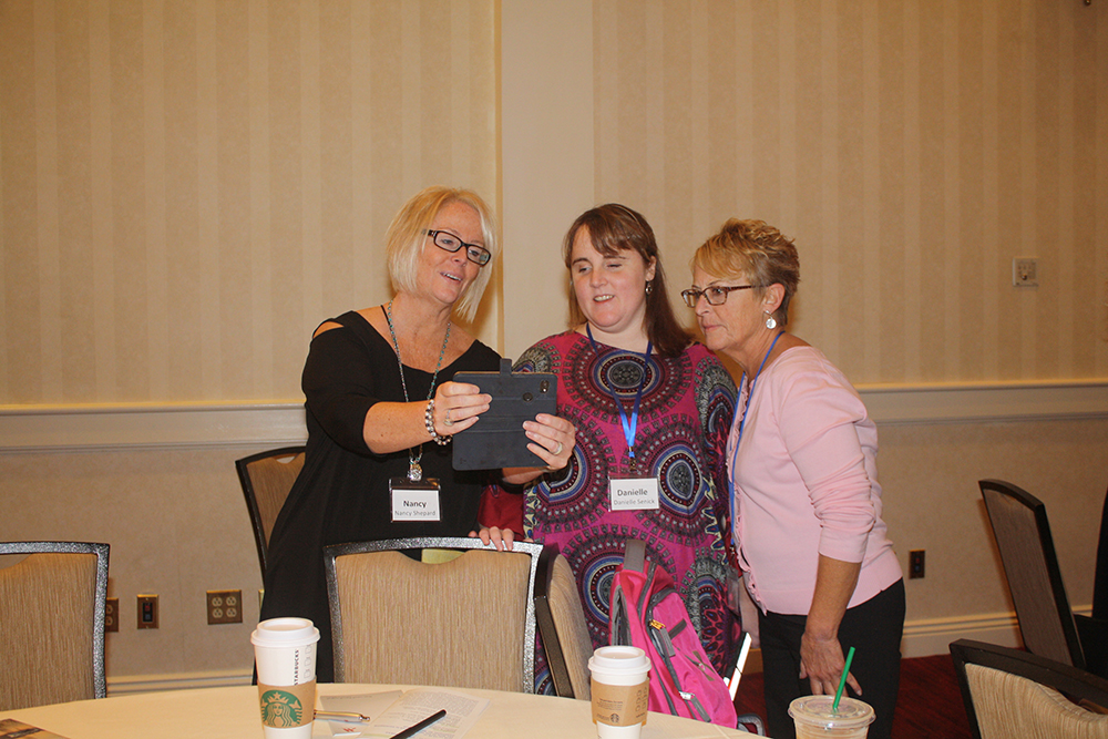 Nancy, Danielle, and Patty with landyards on and looking at a phone that Nancy is holding