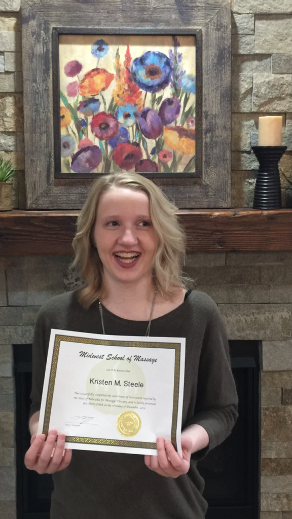Kristen holding up her certificate next to a mantle