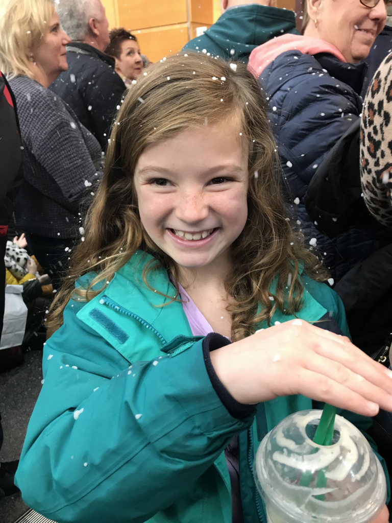 Hannah with a big smile, wearing a light blue green coat and holding a drink