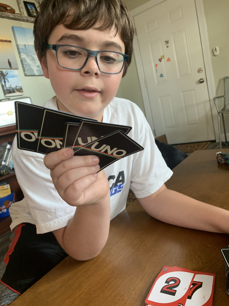 Creed in blue glasses, holding his Uno Cards