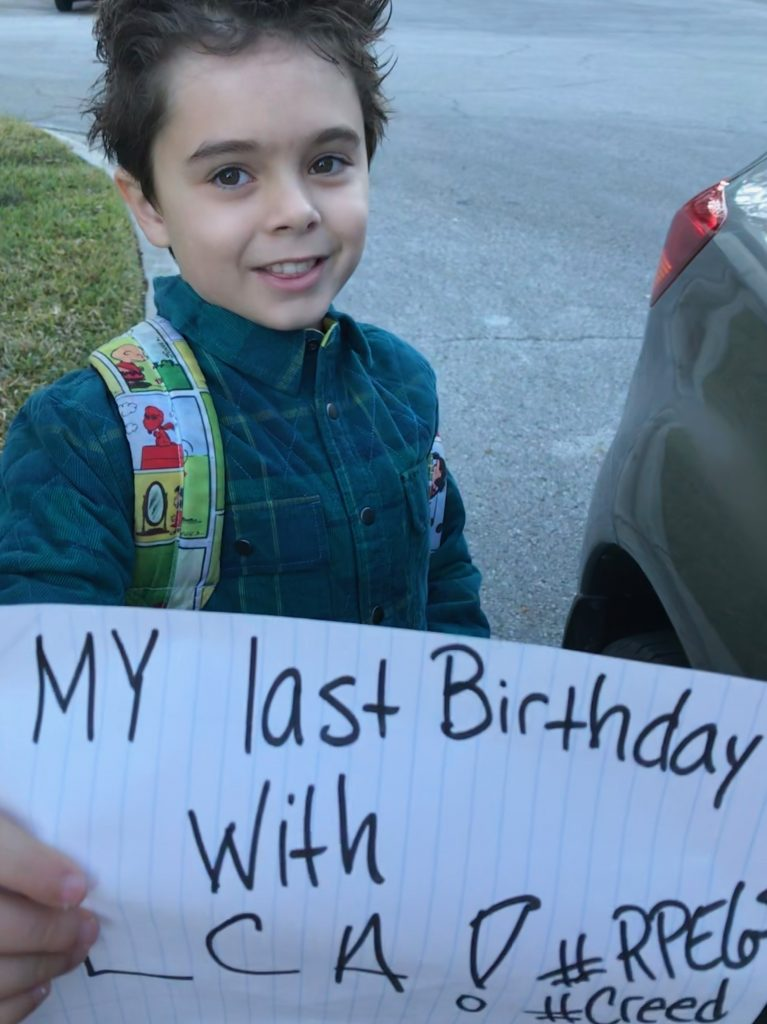 Creed smiling and holding up a piece of paper that writes, "My last birthday with LCA! #RPE65 #CREED
