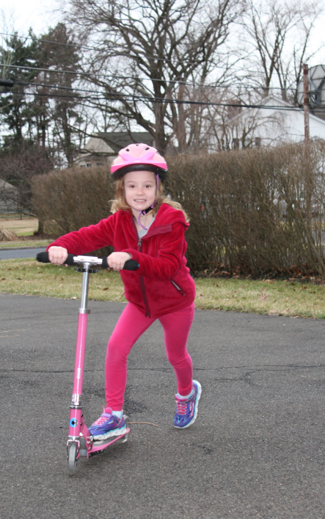 Hannah in red jacket with pink helmet riding her pink scooter.