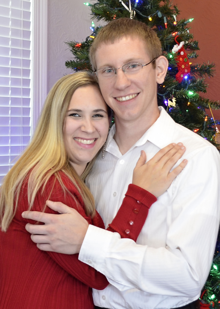 Mikayla in a red shirt and Andrew next to her in a white shirt. There is a Christmas tree in the background