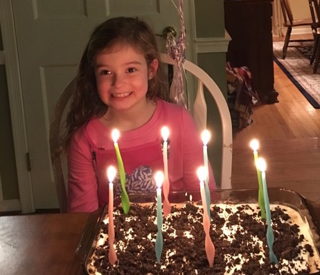 Hannah smiling big with lit birthday candles in front of her