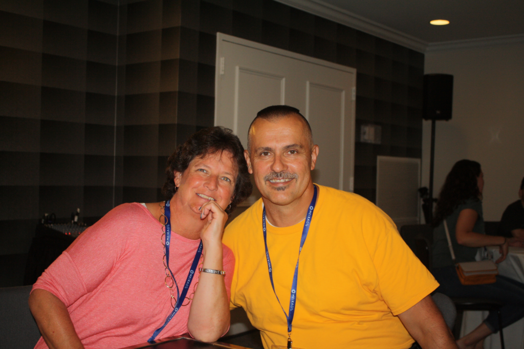 Tami in a pink shirt and Michael besides her in a bright orange shirt sitting at the 2019 LCA Family Conference