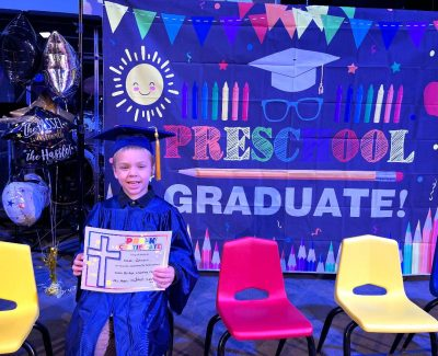 Noah with his graduation cap on holding his certificate with a fun background saying "Preschool graduate!".