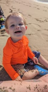 Atlas sitting on the sand wearing a bright orange shirt