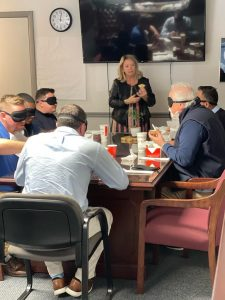 A small group sitting at a table with blindfolds on.