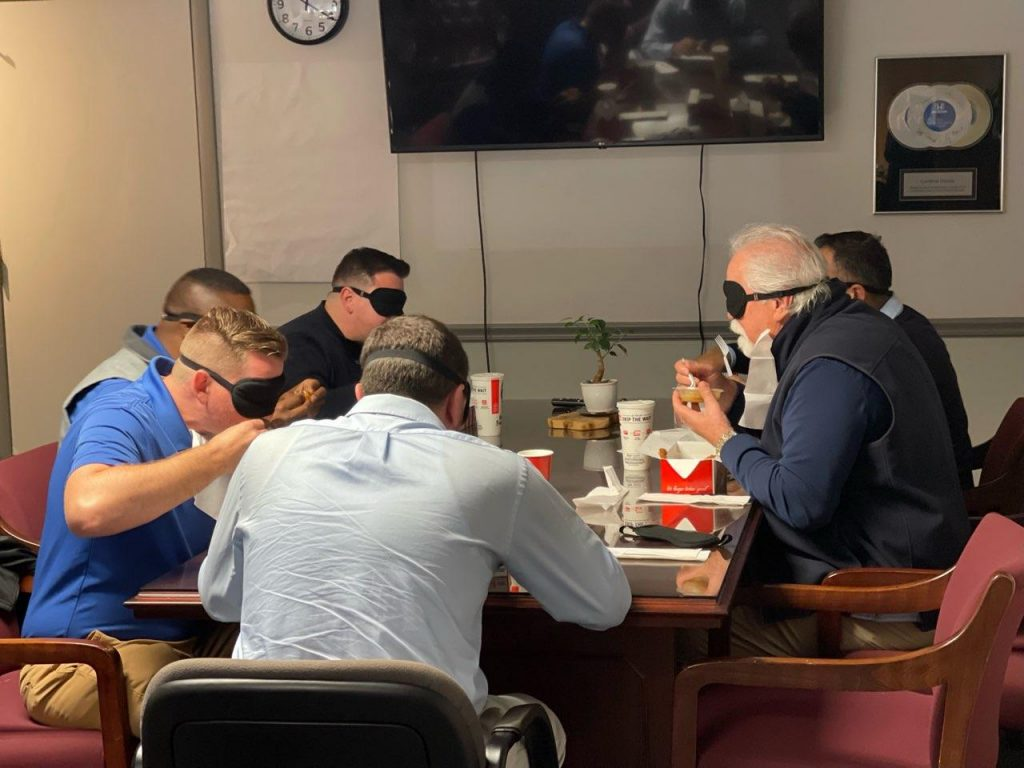 The group blindfolded, sitting at the table and eating.