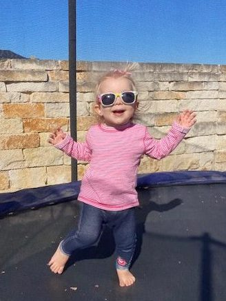 Dylan in a pink stripped shirt and sunglasses, bouncing on her trampoline