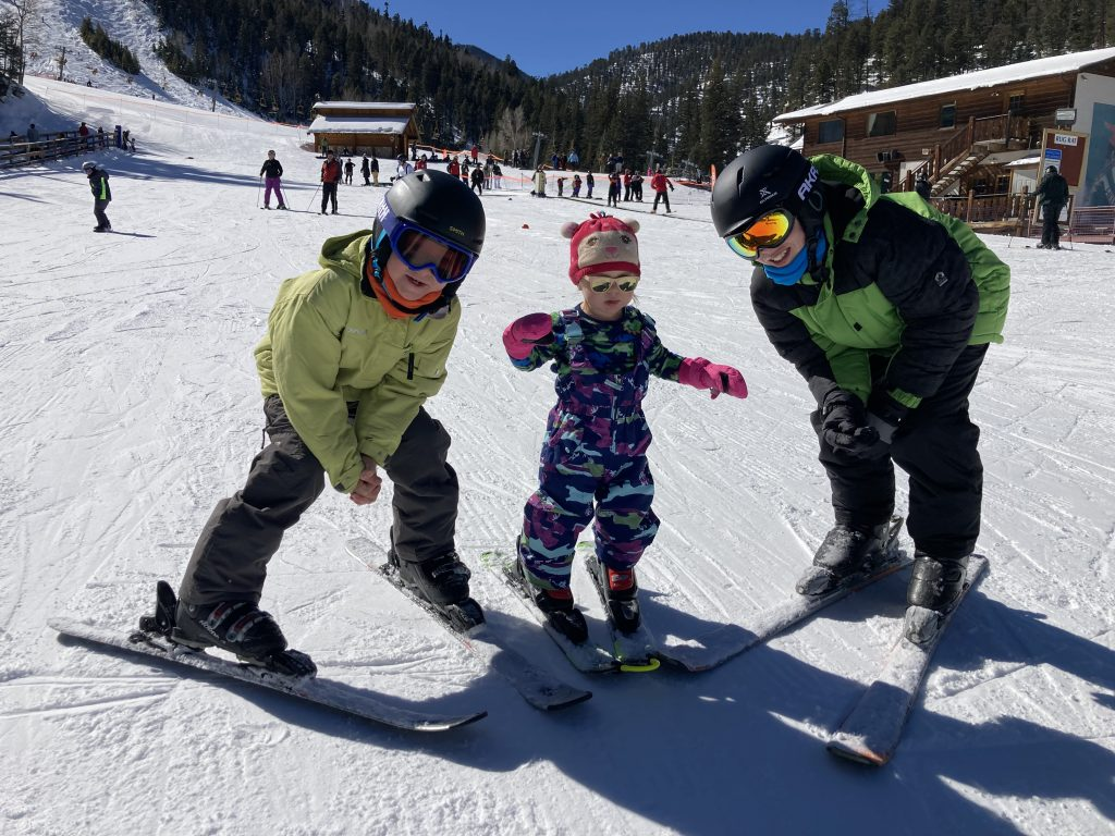Dylan standing in between her brothers with skis on.