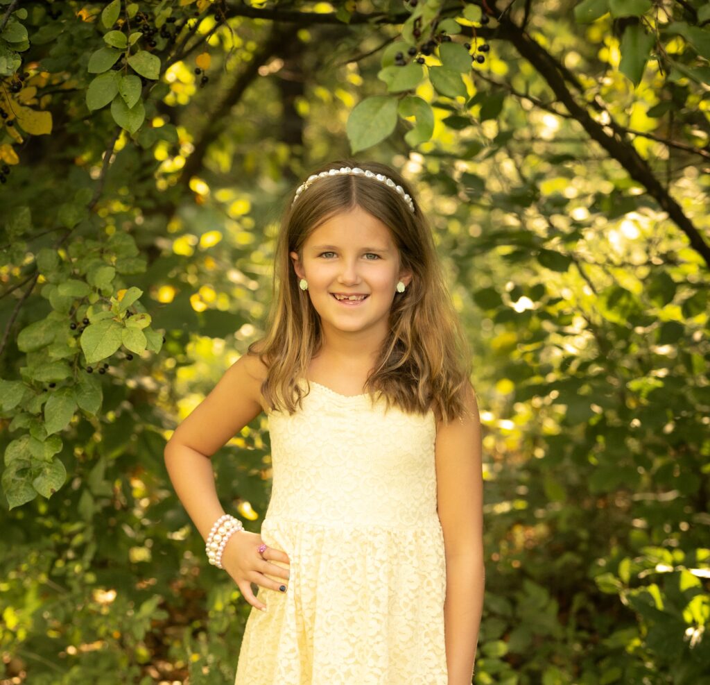 Pepper wearing a yellow dress with a hand on her hip. The background is green and yellow leaves
