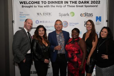 Six Dinner in the Dark attendees in front of the Sponsor banner