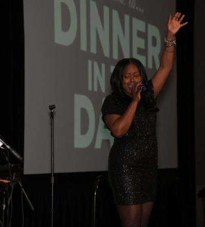 Evelyn Dillion singing with the Dinner in the Dark background behind her